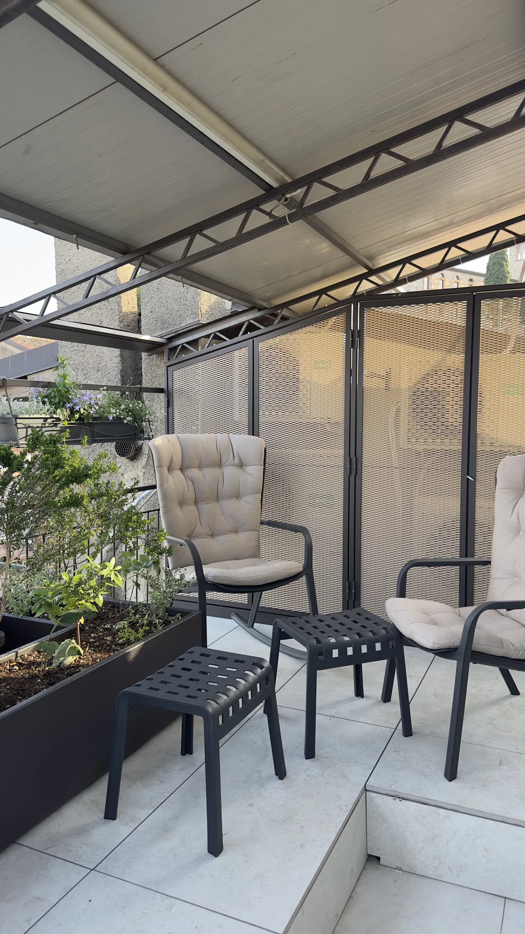 Zona relax su terrazza con pergola a Desenzano del Garda: poltrone in metallo antracite e fioriera