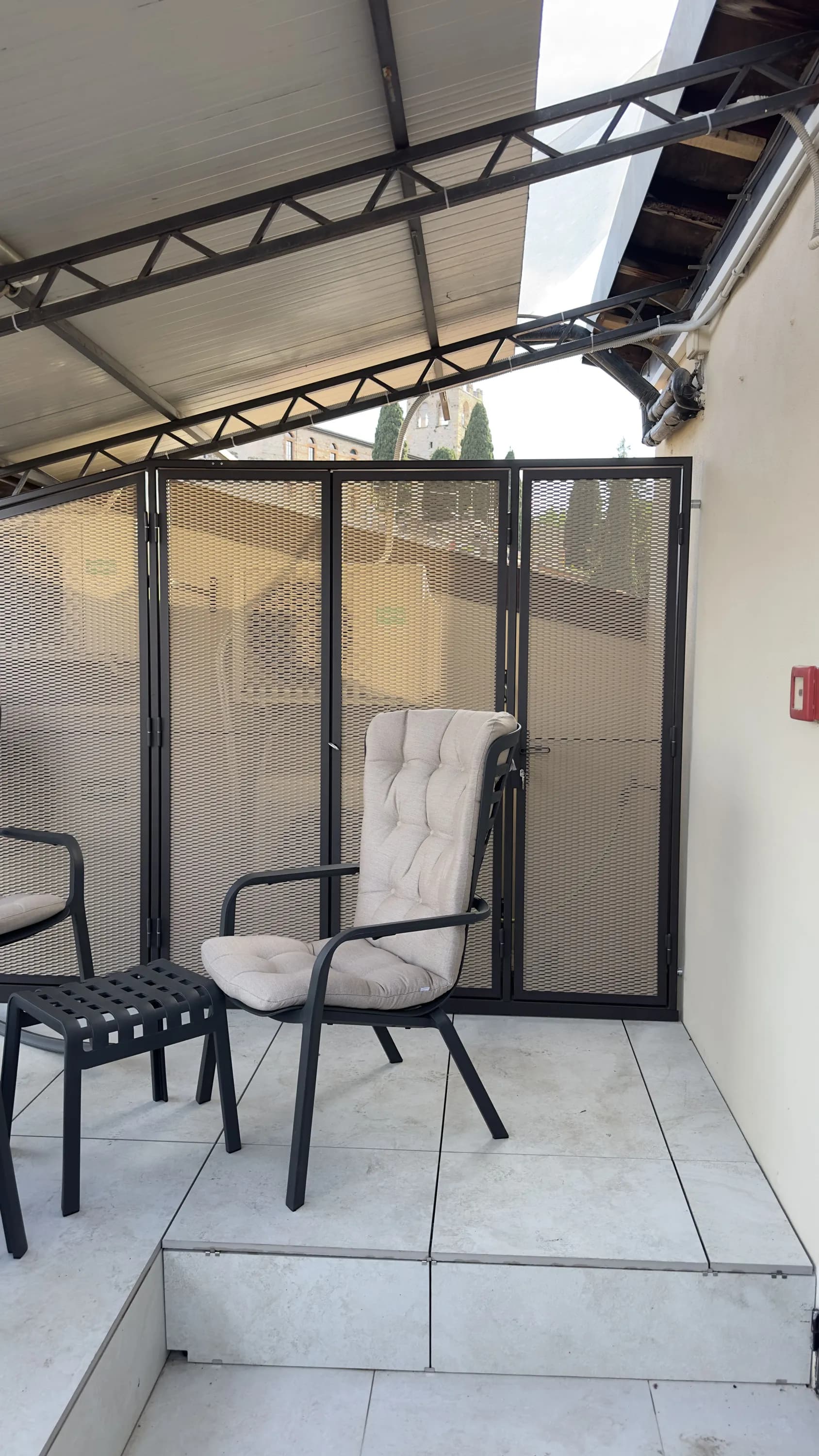Zona relax su terrazza con pergola a Desenzano del Garda: poltrone in metallo antracite e fioriera